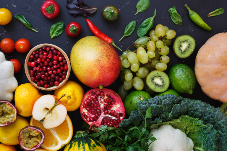 Bunte Auswahl an Obst und Gemüse, darunter Trauben, Mango, Granatapfel und Kräuter.