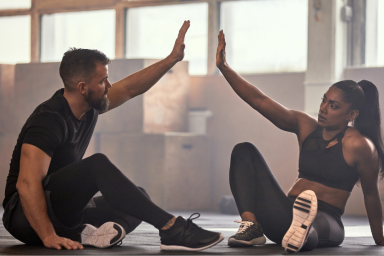 Zwei Personen sitzen auf dem Boden und machen eine Fitnessübung zur Partnerinteraktion.
